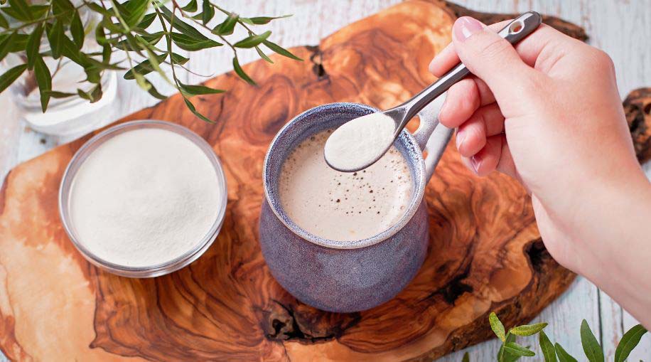 A person adding a spoonful of collagen to their coffee.