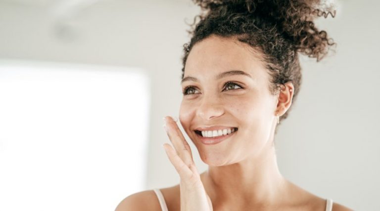 A woman holding her hand near her face, looking at her skin in a mirror