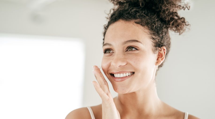 A woman holding her hand near her face, looking at her skin in a mirror