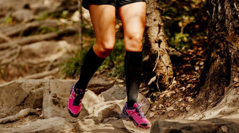 A woman running on a trail, wearing black compression socks and pink shoes.
