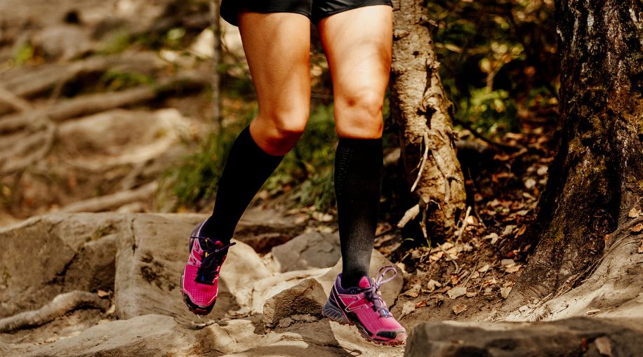 A woman running on a trail, wearing black compression socks and pink shoes.